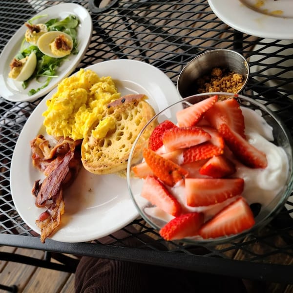 A southern breakfast spread featuring scrambled eggs, bacon, an English muffin, deviled eggs, and strawberries with yogurt.