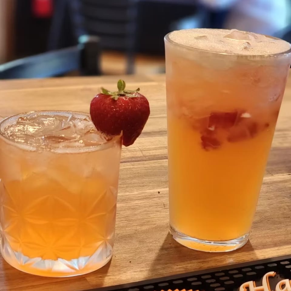 Two refreshing southern-style cocktails, one garnished with a strawberry, on a wooden bar top.