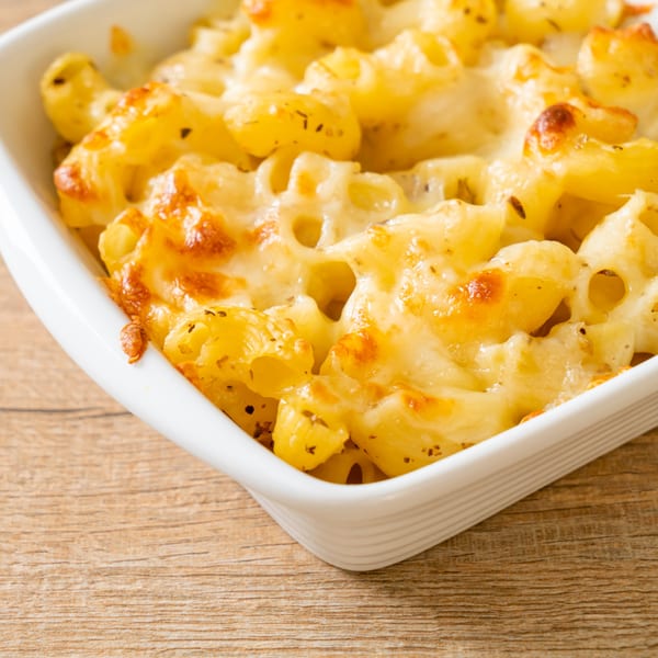 Close-up of baked macaroni and cheese with golden-brown crust in a white dish on a wooden table.