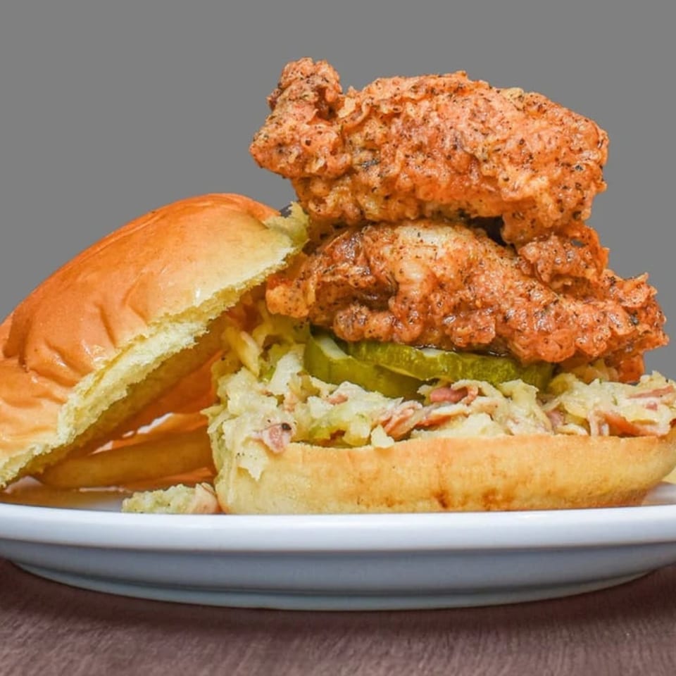Astrid's fried chicken sandwich with pickles and coleslaw on a bun, served with fries.