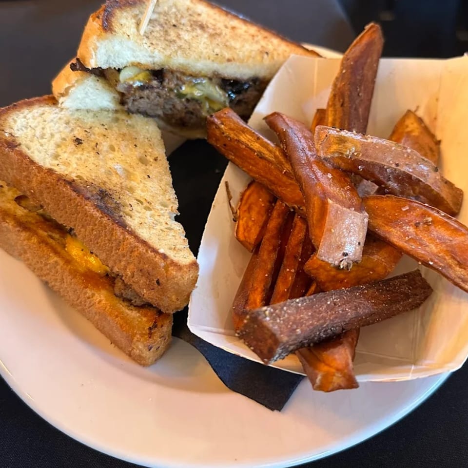 Astrid's southern-style burger with melted cheese and grilled onions, served with a side of sweet potato fries.