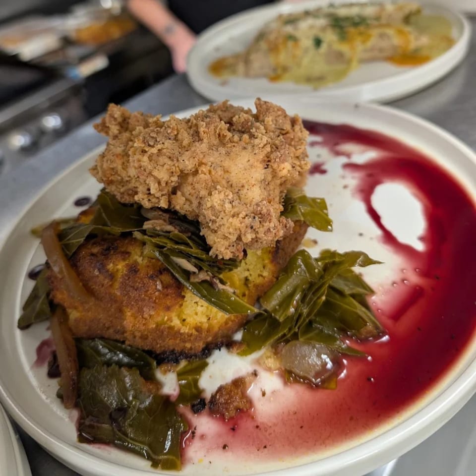 Astrid's fried chicken and collard greens on cornbread with a red sauce, ready to be served.