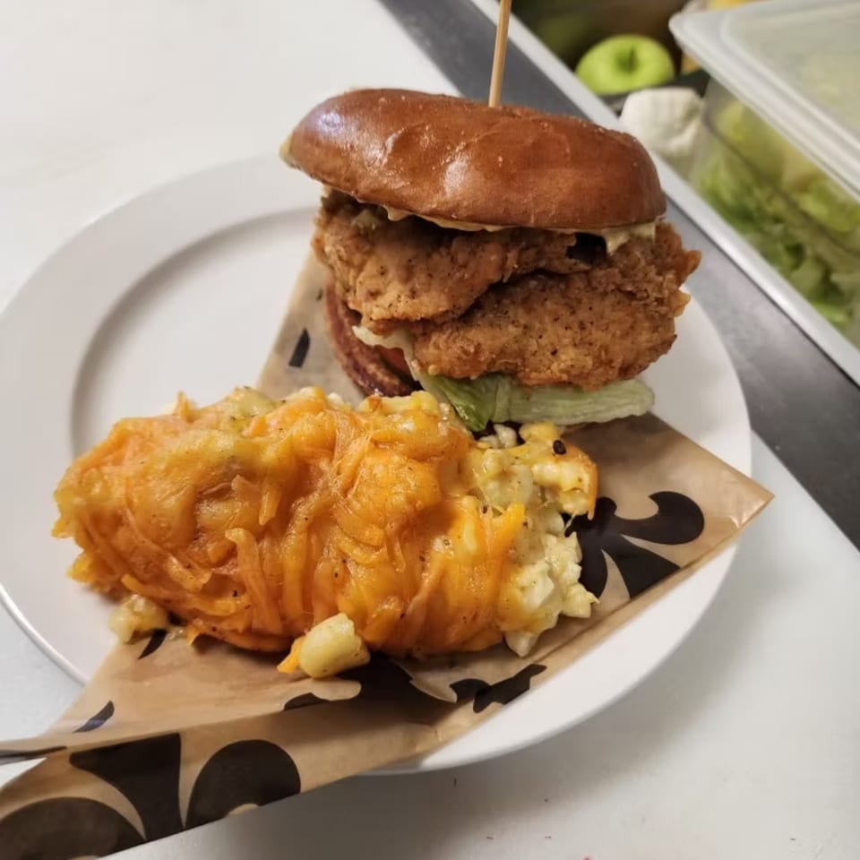 Astrid's fried chicken sandwich with lettuce and a side of cheesy macaroni on a white plate.
